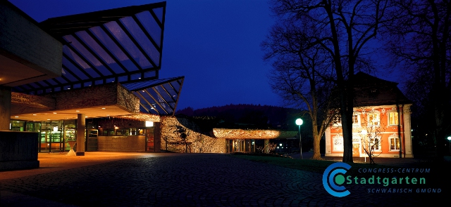 Das Bild zeigt ein modernes Gebäude bei Nacht mit beleuchteten Lichtern und nahen Bäumen unter einem dunklen Himmel.