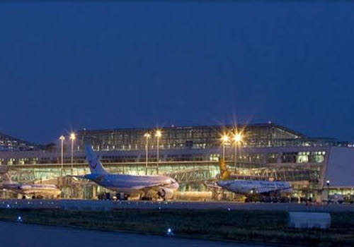 Das Bild zeigt eine Nachtaufnahme an einem Flughafen mit mehreren geparkten Linienmaschinen und beleuchteten Taxiways sowie Terminalgebäuden.