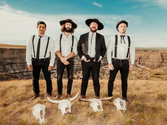 Eine Gruppe von vier Männern mit Cowboyhüten und Jeansanzügen auf der Prärie stehend