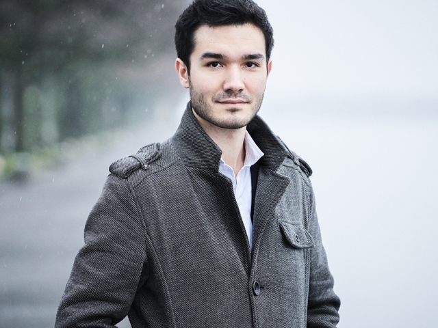 Ein Mann posiert für ein Foto mit offenem Mantel und regennassem, zerzaustem Haar.