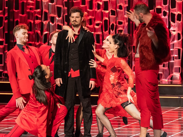 Eine Theateraufführung, bei der Schauspieler in Rot gekleidet sind und Charaktere aus dem Oper "Faust" spielen.