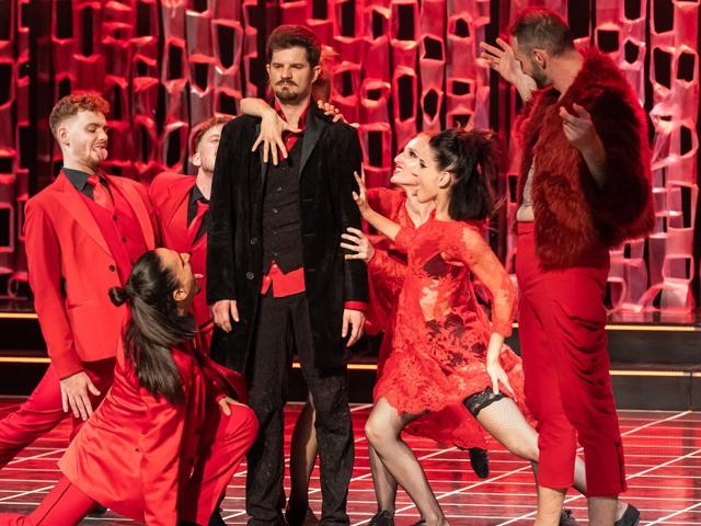 Eine Theateraufführung, bei der Schauspieler in Rot gekleidet sind und Charaktere aus dem Oper "Faust" spielen.