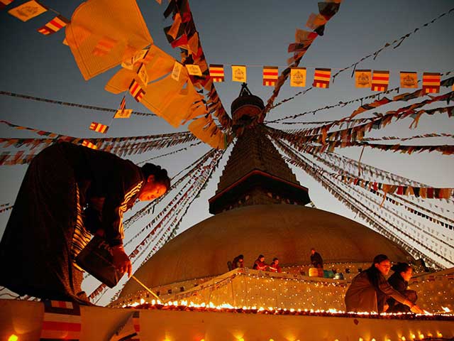 Ein Mann zündet Räucherstäbchen auf einem buddhistischen Gebetsrad bei Einbruch der Dunkelheit an.