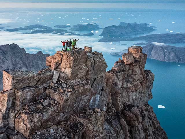 Drei Menschen auf dem Gipfel eines Berges bei Sonnenuntergang, die das Erreichen des Überquerens des Inlandeises von Grönland feiern.