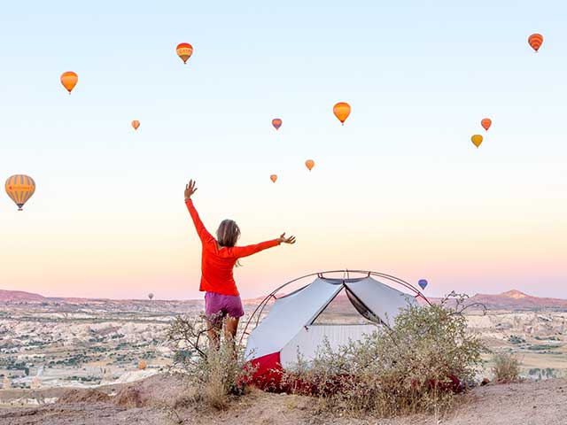 Frau feiernd zwischen Heißluftballons bei Sonnenuntergang