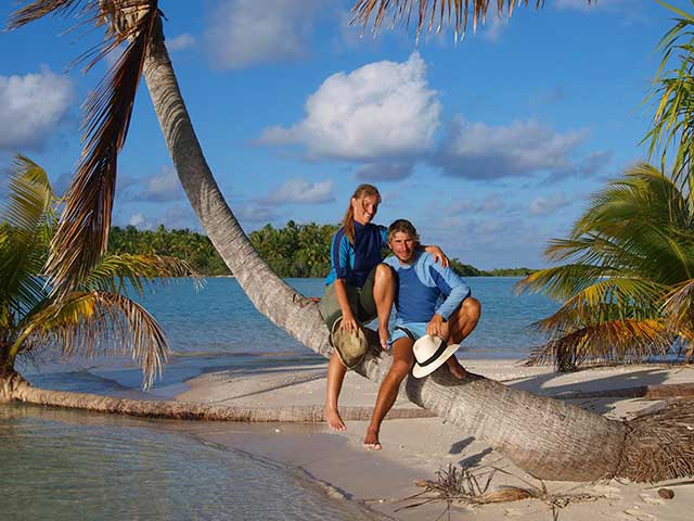 Ein Paar sitzt unter einer Palme auf einer tropischen Insel und trägt Shorts, während es den Tag genießt.
