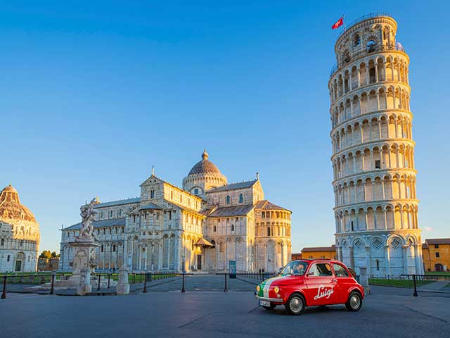 Das Bild zeigt einen roten Fiat 500, der an dem berühmten Wahrzeichen, dem schiefen Turm von Pisa in Italien, vorbeifährt.