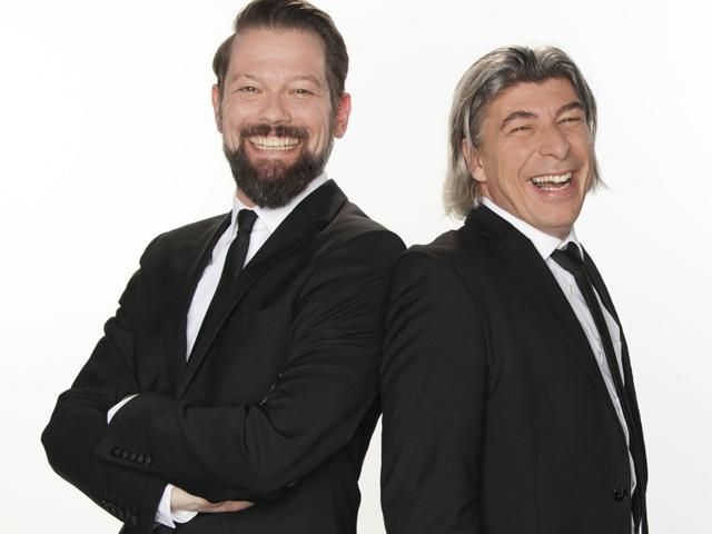 Zwei Männer mit Anzügen und Krawatten, die gemeinsam lachen.