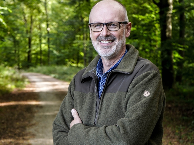 Mann in grüner Jacke auf dem Pfad stehend, der lächelt und selbstbewusst posiert