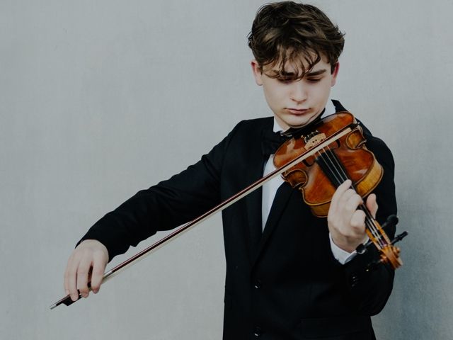 Das Bild zeigt einen jungen Mann, der eine Geige spielt und dabei Abendgarderobe trägt, wahrscheinlich ein Konzerthöhekleidung.