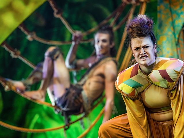 Eine Theateraufführung von Tarzan das Musical, mit Schauspielern kostümiert als Tiere und Menschen in bunten Kostümen.