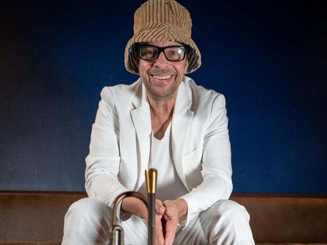 Ein Mann mit einem Weidenhut und Sonnenbrille sitzt auf der Bühne mit einem goldenen Horn.