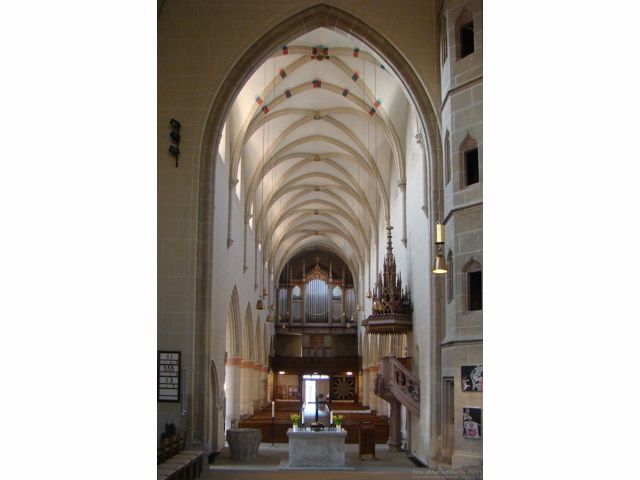 Das Bild zeigt ein großes Kircheninnere im alten Stil mit hohen Bögen und Reihen von Holzpulten.