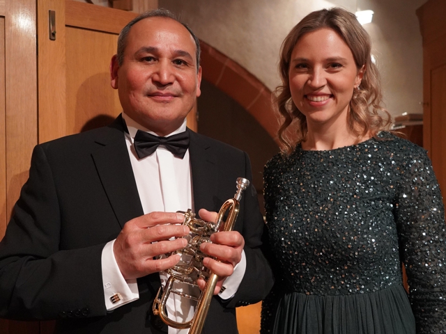 Frau neben einem Mann stehend, der Saxofon spielt und lachend die Hände zusammenschlägt