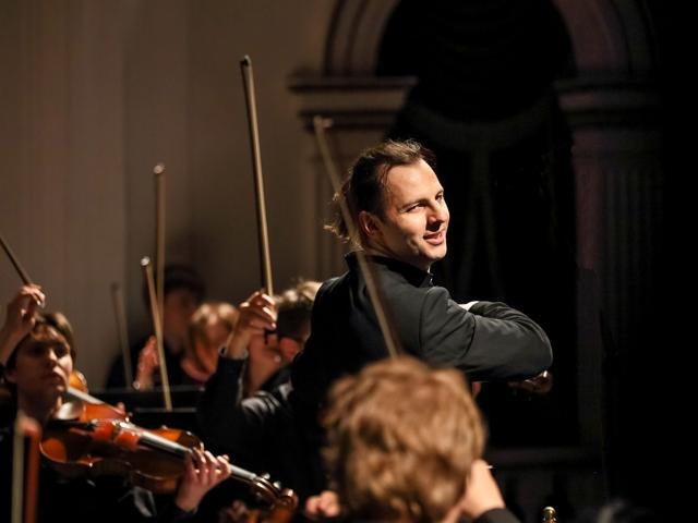 Leitender Musiker lächelt während einer Symphonie-Aufführung ins Publikum.